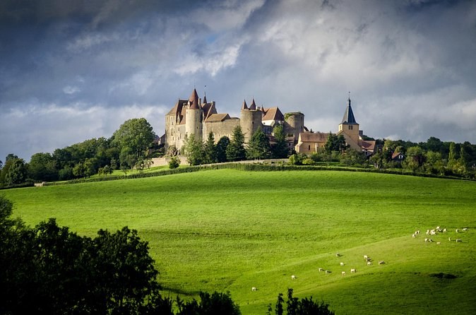 A turreted château on a wooded hilltop above green pasture