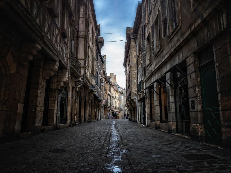 A narrow street of tall stone houses, its paving wet after rain